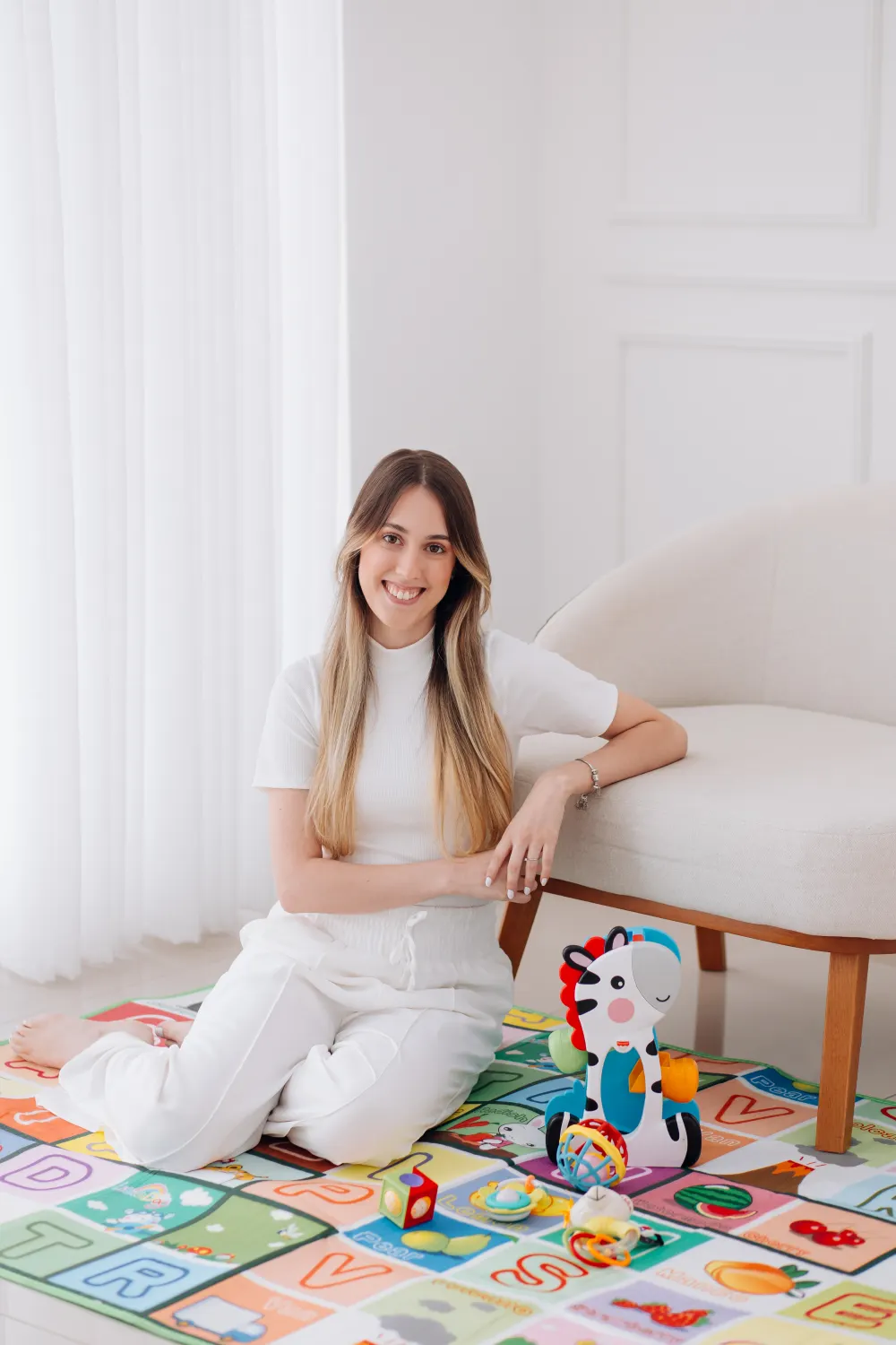 Anna Pataro, fisioterapeuta infantil, sentada no tapete de atividades como no atendimento domiciliar