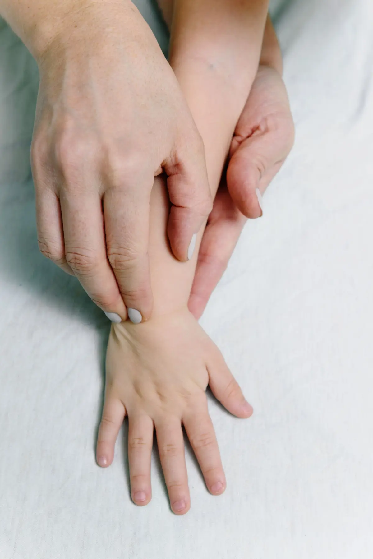 Fisioterapia infantil a domicílio: mãos da fisioterapeuta cuidando da mãozinha do bebê